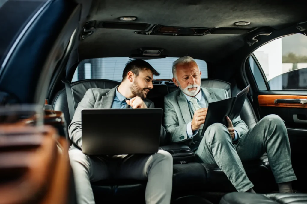 Two professionals in a luxury limousine with a laptop showcasing corporate travel services in NYC