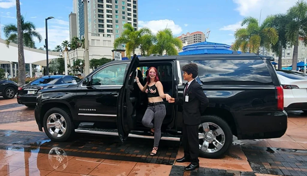 Cheuffer hold hand of woman that coming out form a black SUV, representing a Florida travel limo rental service