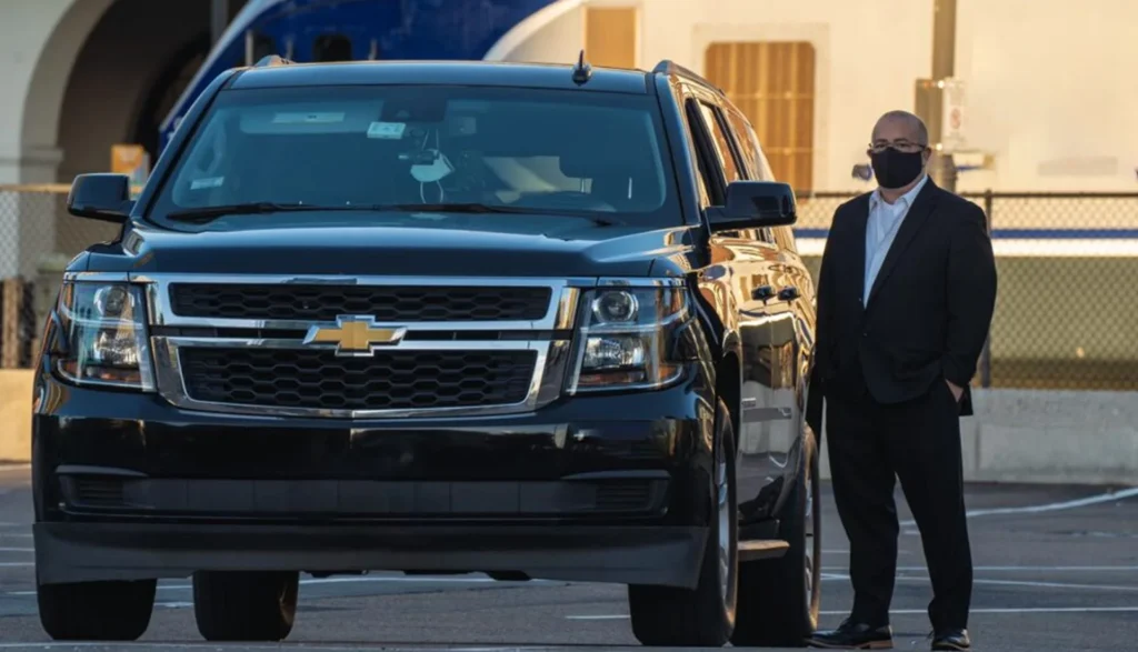 Man in a face mask stands beside a black Chevrolet SUV, representing LAX black car service
